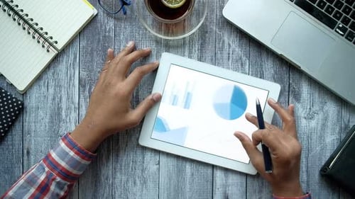Man's Hand Working on Digital Tablet at Office Desk Using Self Created Chart