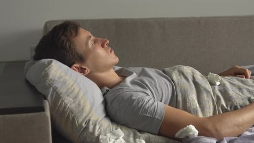 Sick Man Blowing Nose While Lying in Bed