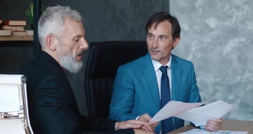 Mature Male Colleagues Discuss Business Sitting at the Table in the Office