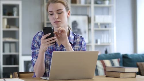 Woman Using Phone While Working at Laptop