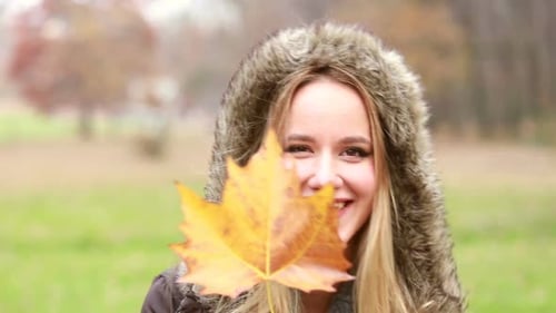 Woman Hiding Behind Autumn Leaf Smiling in Park