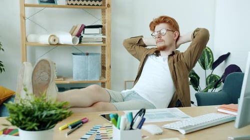 Junger Mann, Freelancer, sitzt im Sessel und denkt entspannt über die Arbeit drinnen in der Wohnung nach