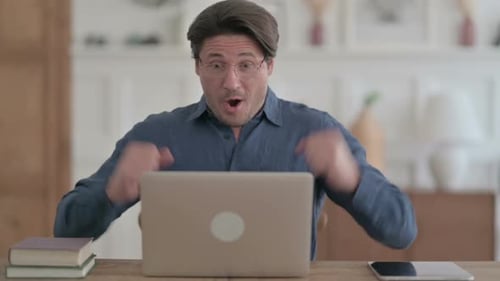 Young Man Celebrating Success while using Laptop in Office