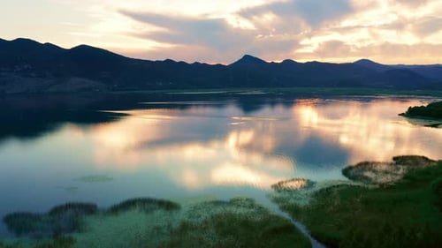 Beautiful sunset sky reflected in lake - marsh grass and silhouettes of mountains.