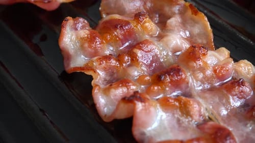 Fried bacon slices rotate in a grill pan.