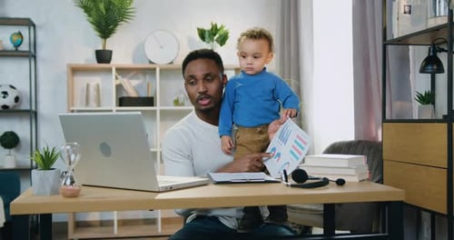 Padre que se quedó en casa con su hijo pequeño y hablando con sus colegas a través de una videoconferencia