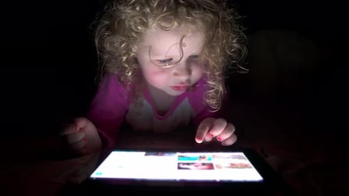 Gros plan d'une adorable fille aux cheveux bouclés de quatre ans utilise une tablette la nuit au lit.