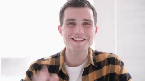 Young Man Waving at Camera Indoors