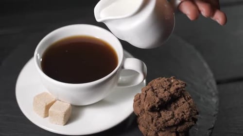 Pouring Milk into Coffee Next to Chocolate Cookies