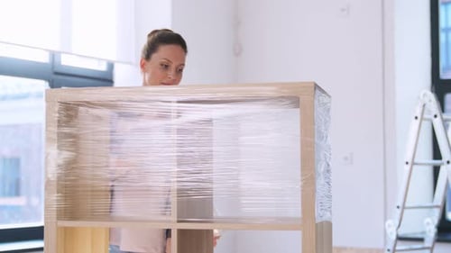Woman Packing Shelf with Plastic Wrap at Home