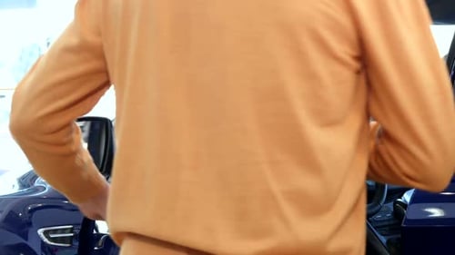 Senior Man Sits Down Into the Car at the Dealership