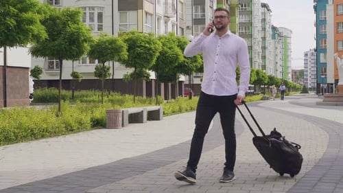 Man Talking on Phone While Pulling Suitcase Outdoors