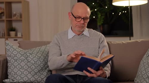Senior Man Reading Book on Couch at Home