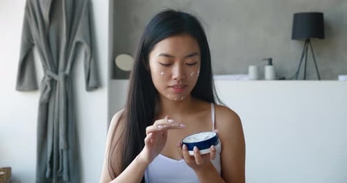 Woman Applies Face Cream in Bathroom, Beauty Routine