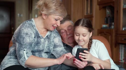 Girl Uses Mobile Phone with Grandparents Indoors