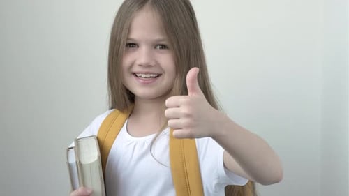 Portrait of Smiling School Girl in White Tshort with Yellow Backpack and Books Making Giving Thumb