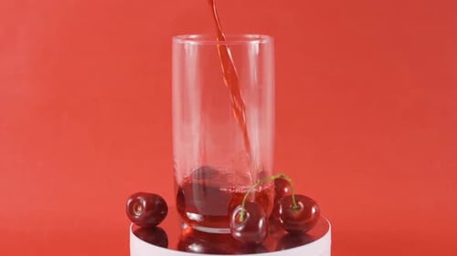 Cherry Juice Poured into Glass with Red Background