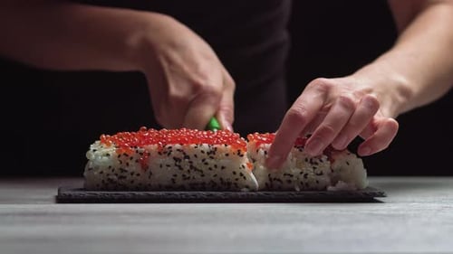 Chef Cutting Rolls of Sushi with a Knife on a Stone Board. - Shot at a Low Angle