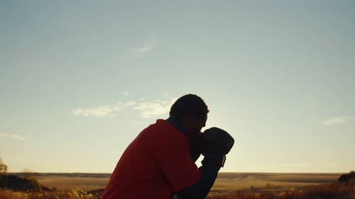 Black Man in Boxing Gloves is Boxing Outdoors Against Background of Sun Side View