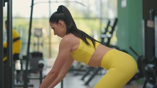 Eine junge hispanische Frau in einem gelben Trainingsanzug führt eine Übung in einem Crossover durch und zieht ein Stahlseil