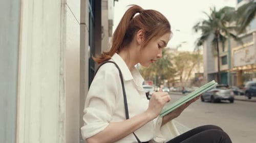 Businesswoman using digital tablet and typing text message while sitting alone outdoor in city.