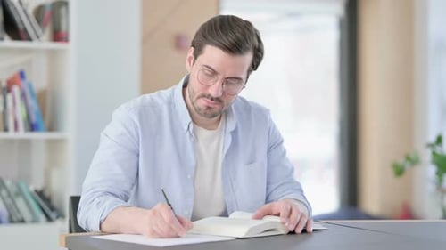 Mann mit Brille liest Buch und macht sich Notizen