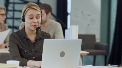Smiling Female Helpline Operator with Headphones at Her Desk in the Office