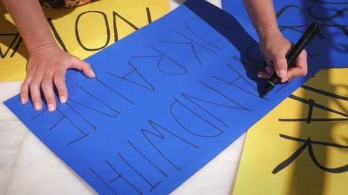 Girl making blue placard Stand With Ukraine at peaceful protest against war.