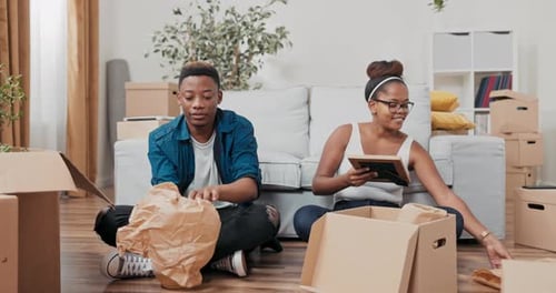 Young People in Love Move Into a New Apartment Sit on the Floor and Pack Their Things Into Boxes