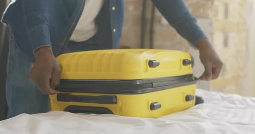 Person Zipping Yellow Suitcase on Bed