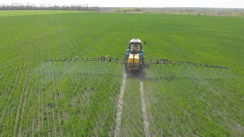Aerial View of Farming Tractor Spraying on Field with Sprayer, Herbicides and Pesticides at Sunset