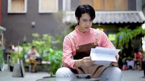 Bored anxiety Asian man small business owner making income and expenditure accounts to check costs