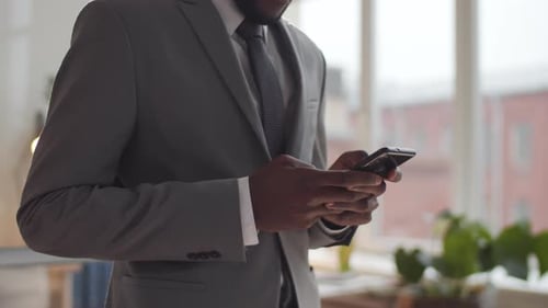 Midsection Shot of Black Businessman Standing in Office and Using Smartphone