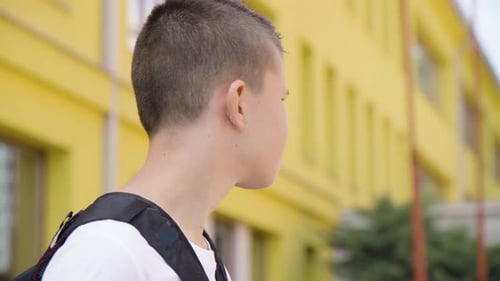A Caucasian Teenage Boy Looks Around in Thought Side Closeup a School in the Background