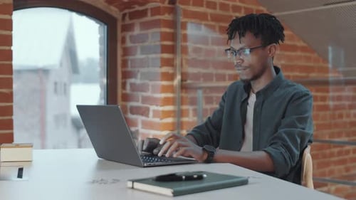 African American Man Working on Laptop in Loft Office