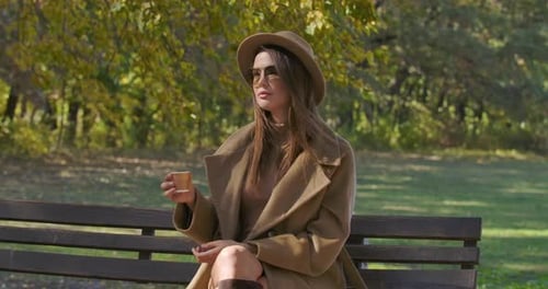 Woman With Hat Drinks on Park Bench