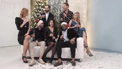 Grupo de jovens amigos bebendo champanhe sentados no sofá durante a festa de ano novo em casa