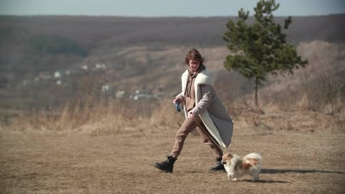 A Young Girl is Walking Fast with a Small Pomeranian Spitz on a Spring Hill
