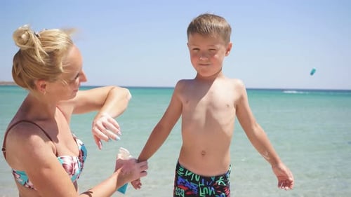 Porträt einer Mutter, die sich um ihren Sohn kümmert, einer Frau, die Sonnenschutzlotion auf die Haut des Babys aufträgt