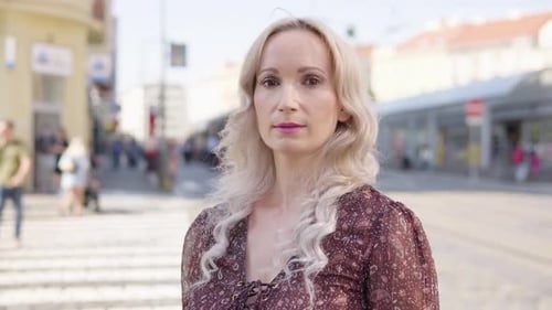 A Middleaged Caucasian Woman Looks Seriously at the Camera in an Urban Area
