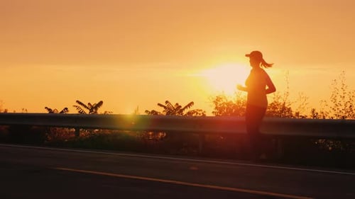 A Young Woman Runs Along the Road Along the Seashore at Sunset. Silhouette