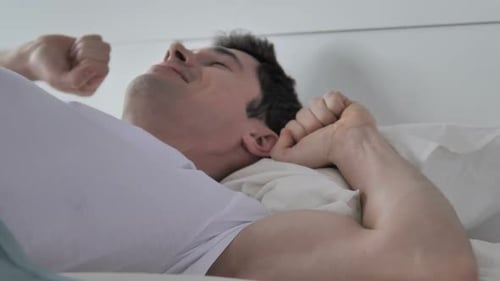Man Wakes Up and Stretches in White Bed