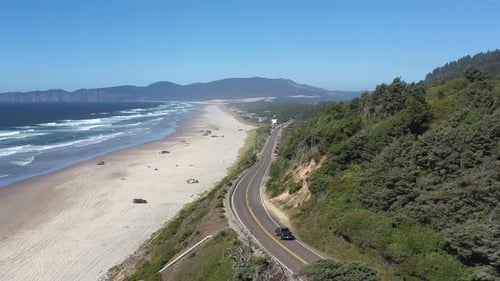 Aerial follow of car driving on scenic road next to the beach with beautiful nature around it.