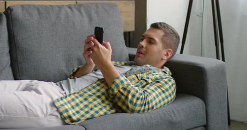 Handsome Man Lying on Couch, Browsing in Mobile Phone