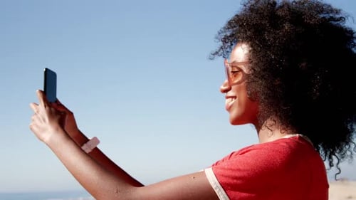 Woman taking selfie with mobile phone on beach in sunshine 4k