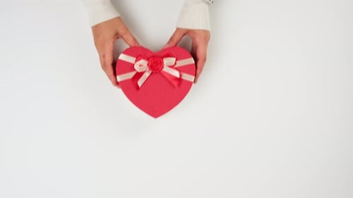 Hands Presenting Red Heart-Shaped Christmas Gift
