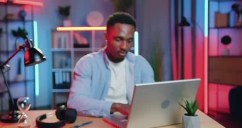 Young Man Works on Laptop in Neon Lit Office
