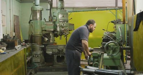 Caucasian male factory worker at a factory sitting at a workbench and operating machinery