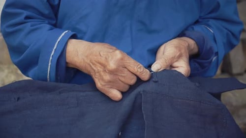 Elderly Hands Repairing Dark Blue Linen Clothing