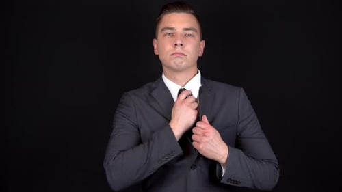 Man in Suit Adjusting Tie on Black Background